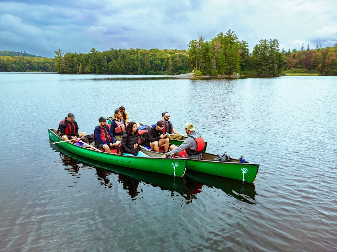 Group of people in a green canoe on a calm lake with trees in the background