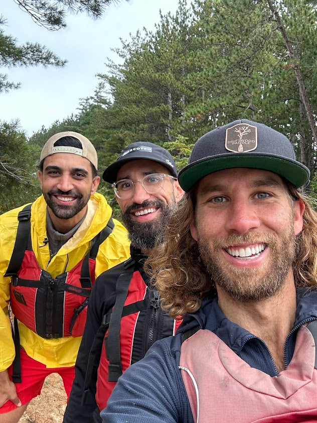 Three men posing for a selfie outdoors with trees in the background
