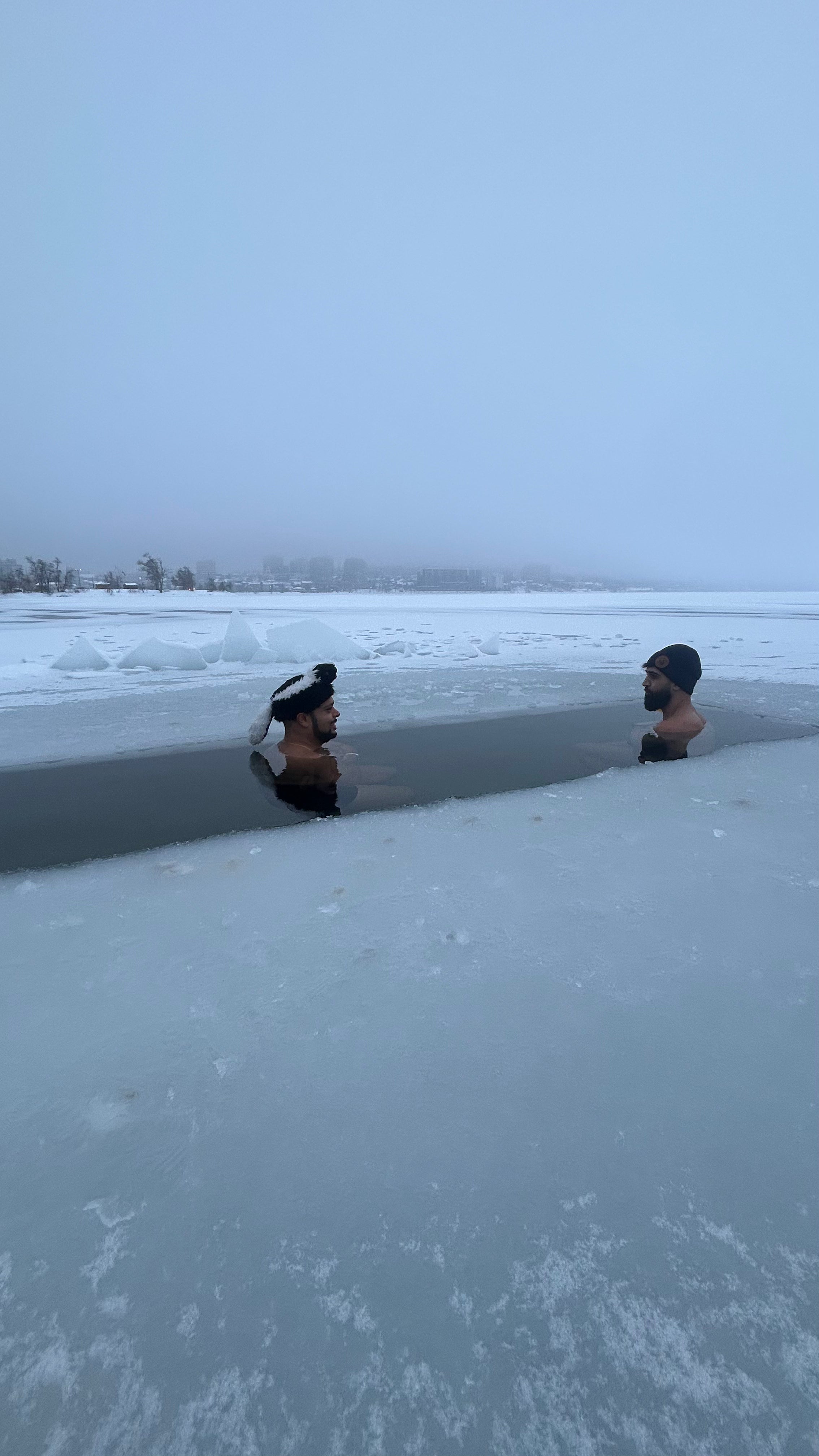 Two people cold plunging on a snowy landscape.