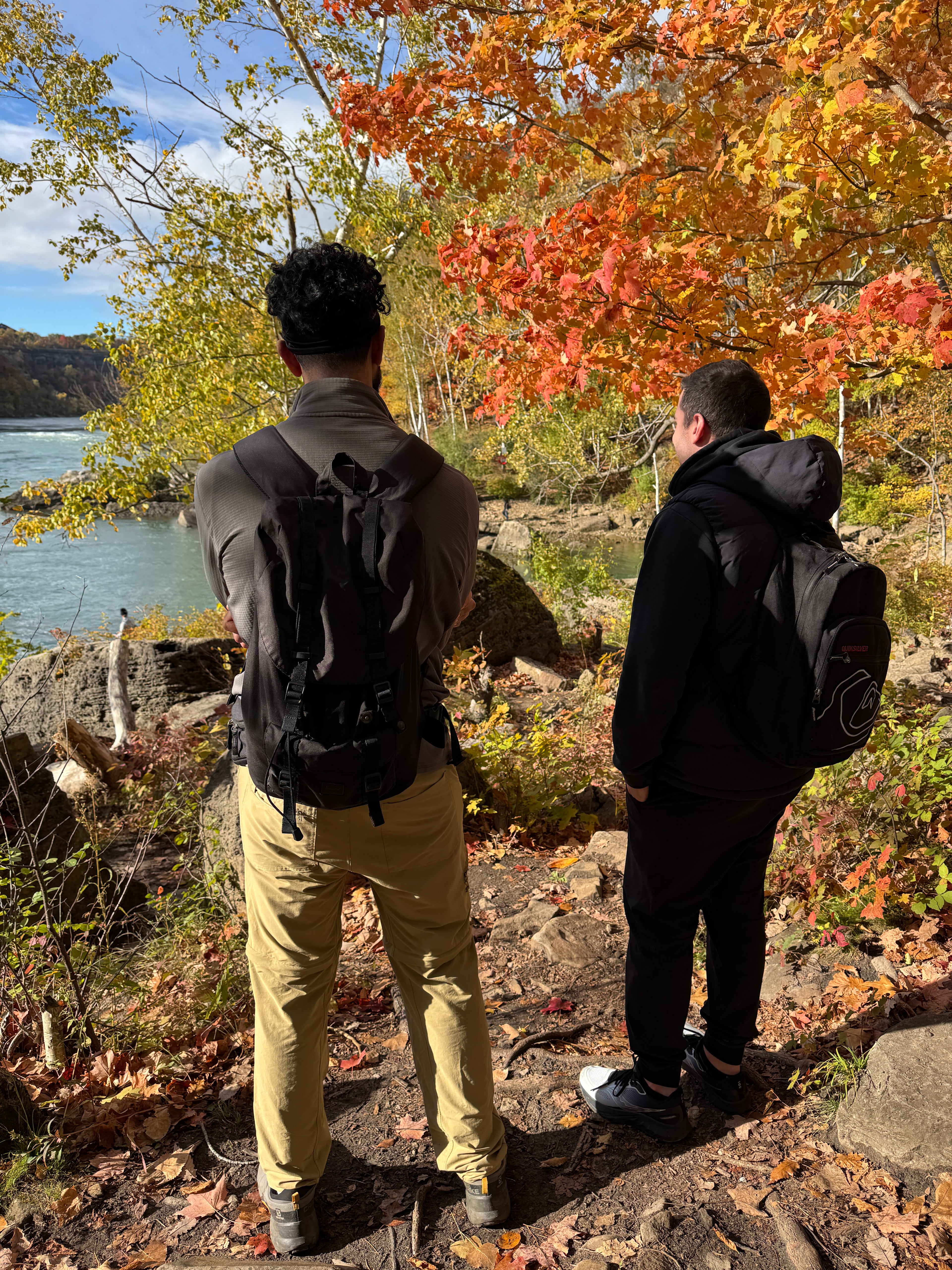 Two people standing on a rocky path with autumn foliage and a lake in the background